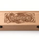 The Designcraft Studio 1-row wooden card box in cherry, with a custom dragon and NerdSnack engraving on the lid and two antique brass latches