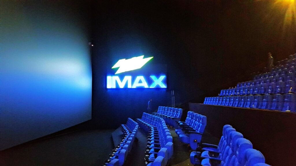 An IMAX movie theater auditorium with blue seats and the IMAX logo glowing beside the screen