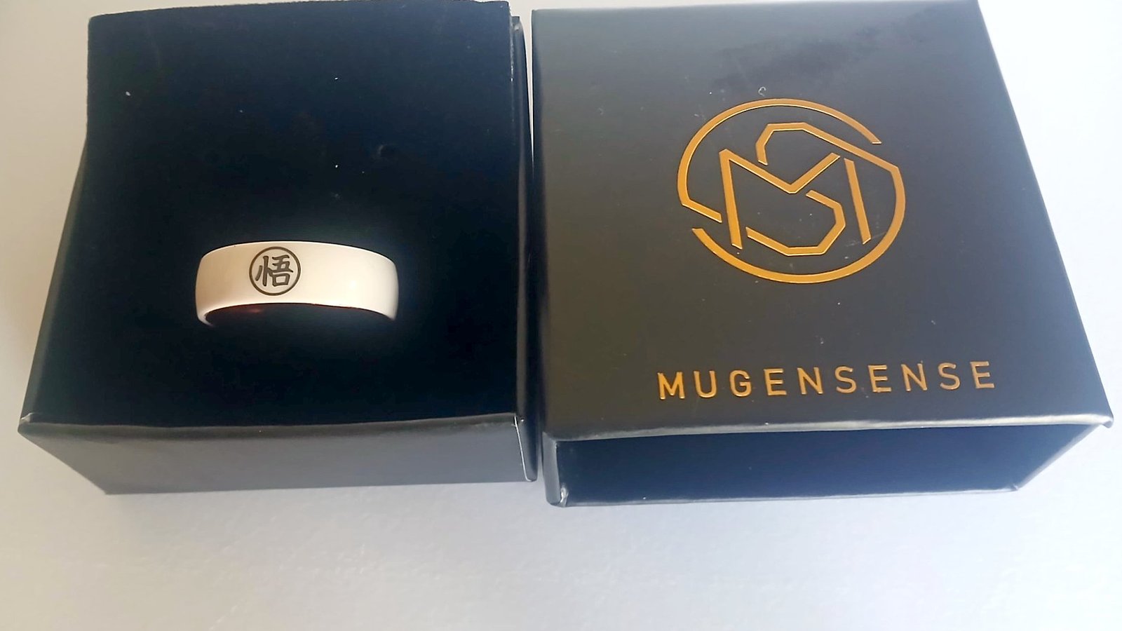 The MugenSense Son Goku ring in its velvet-lined box next to the lid with the gold MugenSense logo