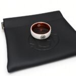 The MugenSense Son Goku ring, white titanium with the Go kanji and an orange inner band, resting on its black logo pouch