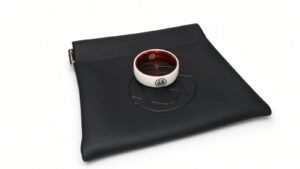The MugenSense Son Goku ring, white titanium with the Go kanji and an orange inner band, resting on its black logo pouch