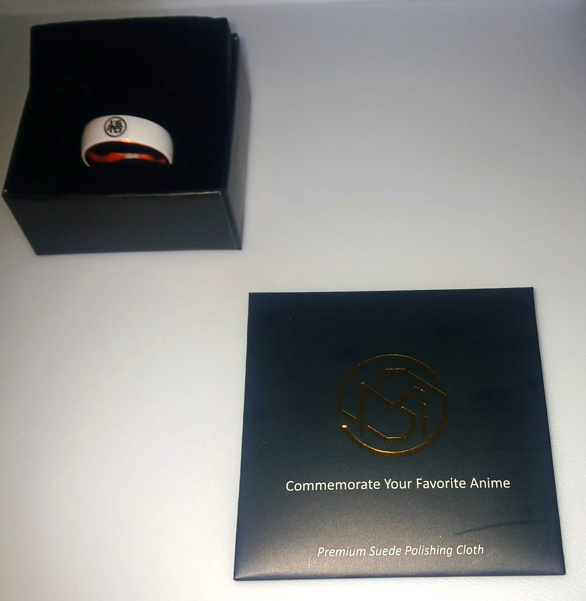 The MugenSense Son Goku ring in its box above the branded Premium Suede Polishing Cloth sleeve