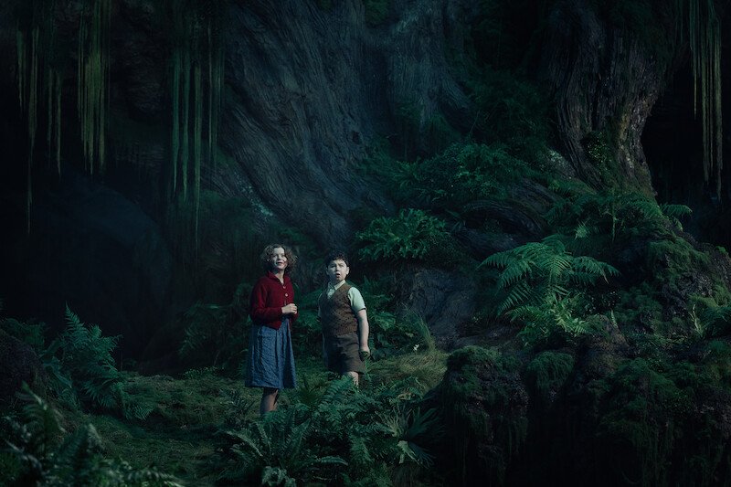 Digory and Polly in a green forest cave in a first-look still from Narnia: The Magician’s Nephew